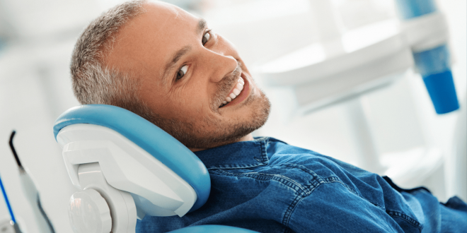 Uomo sorridente seduto sulla poltrona del dentista durante una visita