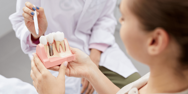 una bambina tiene in mano il modello di un impianto dentale e la dentista le spiega la struttura