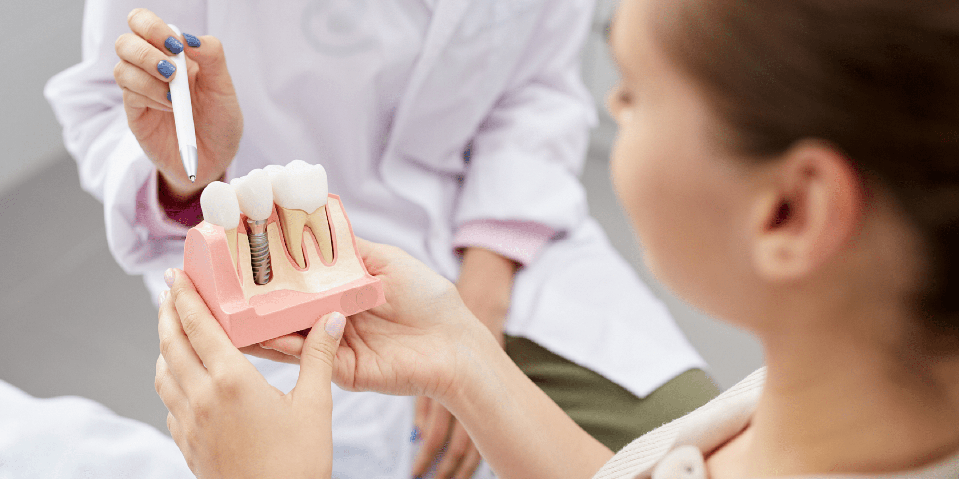 una bambina tiene in mano il modello di un impianto dentale e la dentista le spiega la struttura