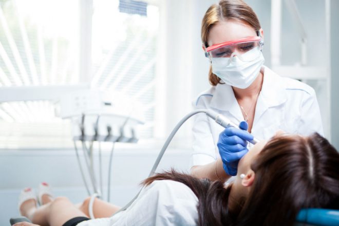evoluzione-igienista-dentale Igienista dentale con mascherina e occhiali protettivi esegue una seduta di igiene orale professionale su una paziente