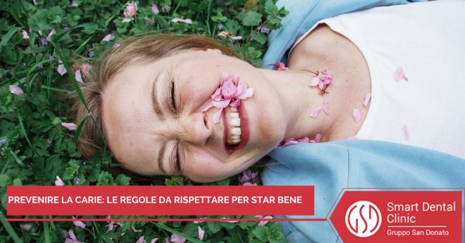 prevenzione-carie Donna che sorride sdraiata sull'erba con fiori sul viso